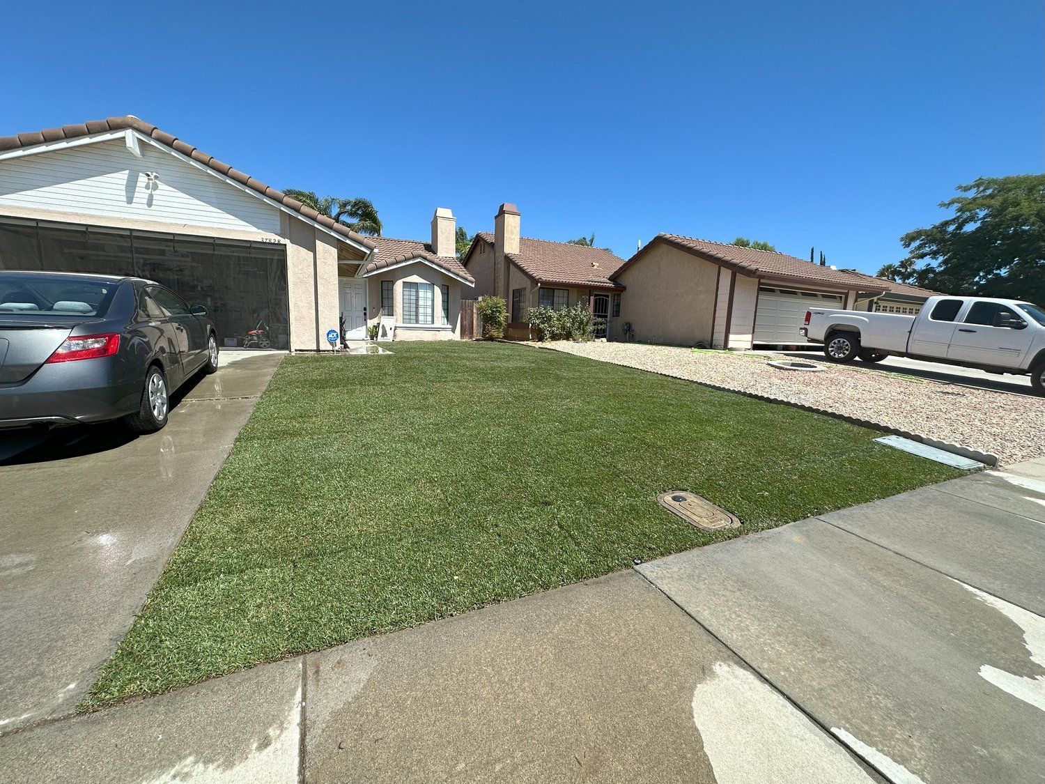A car is parked in front of a house with a truck parked in the driveway.
