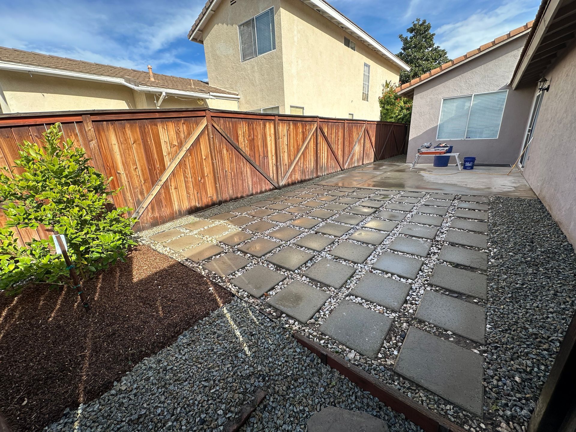 A patio with a wooden fence and gravel in front of a house.