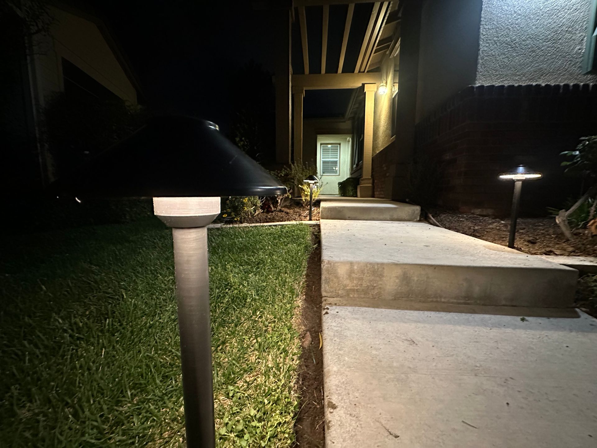 A concrete walkway with lights on the side of it at night.