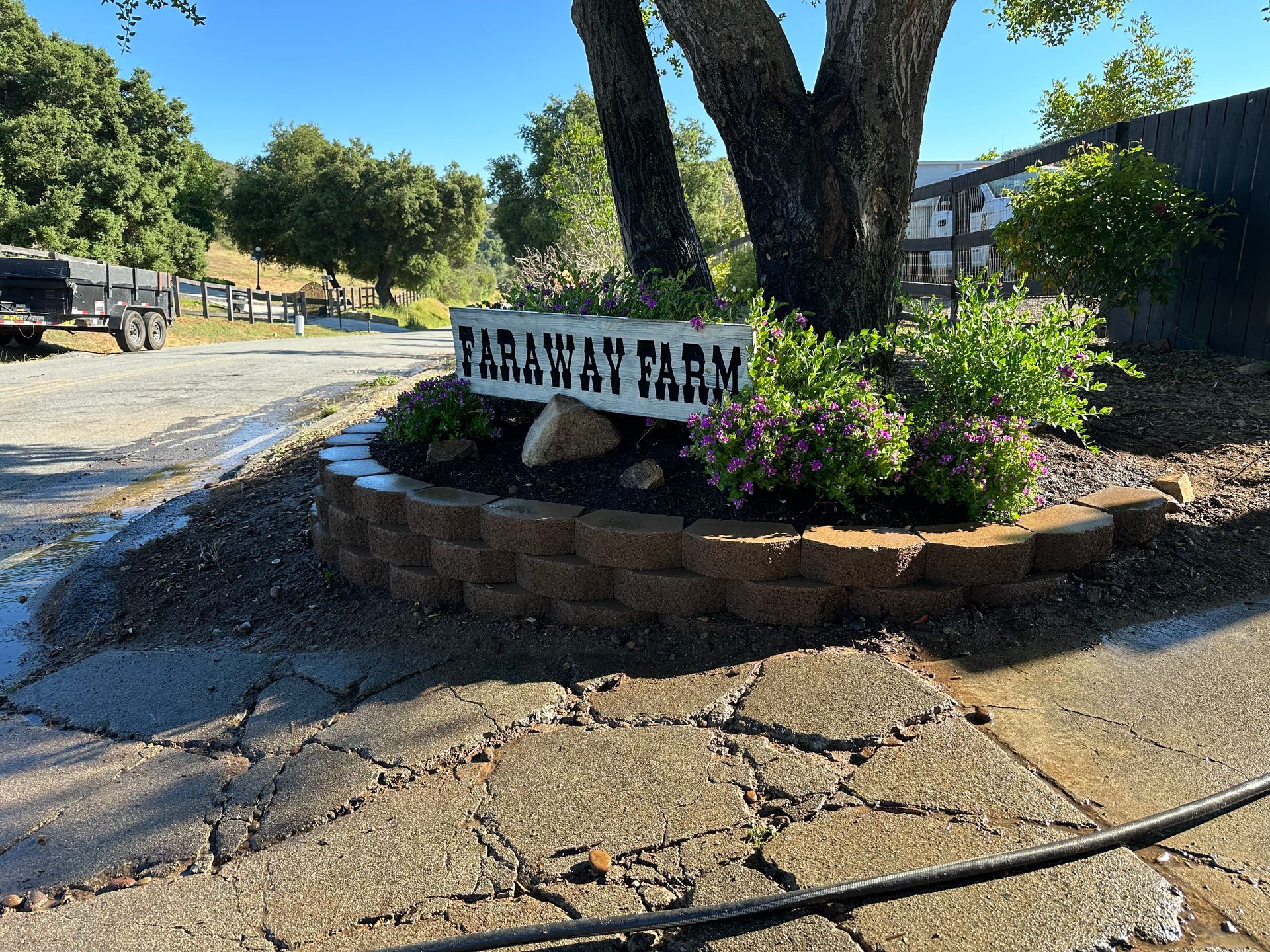 A sign for a farm is sitting under a tree.