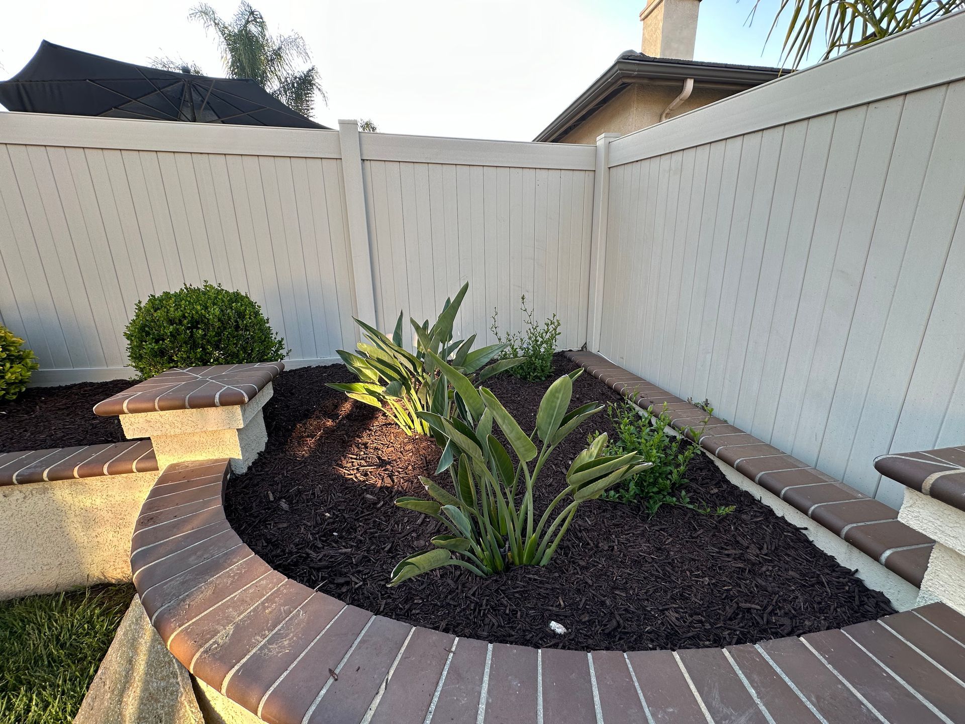 A white fence surrounds a planter with plants in it