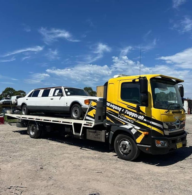 A Yellow Tow Truck With a White Car on the Back of It — Wyong and Tuggerah Towing Service in Tuggerah, NSW