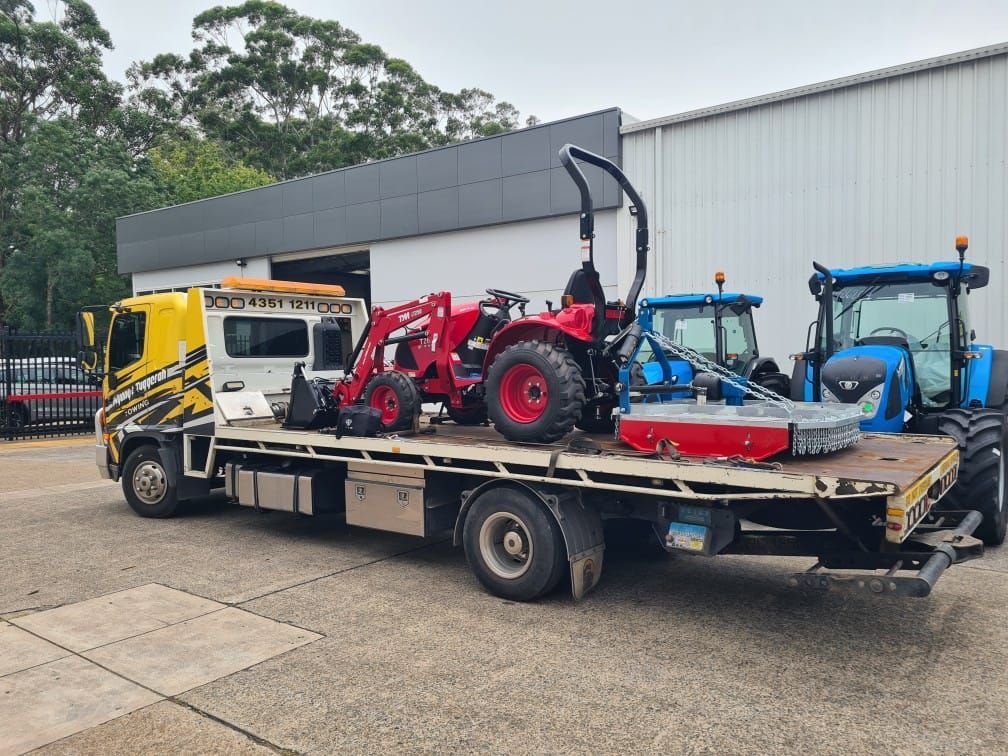 A Tow Truck is Carrying a Tractor on the Back of It — Wyong and Tuggerah Towing Service in Tuggerah, NSW