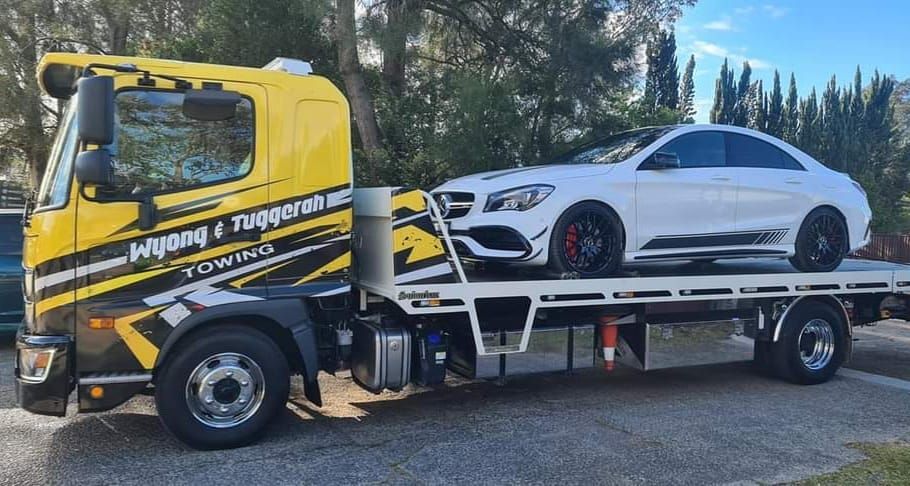A Yellow Tow Truck With a White Car on the Back of It — Wyong and Tuggerah Towing Service in Tuggerah, NSW