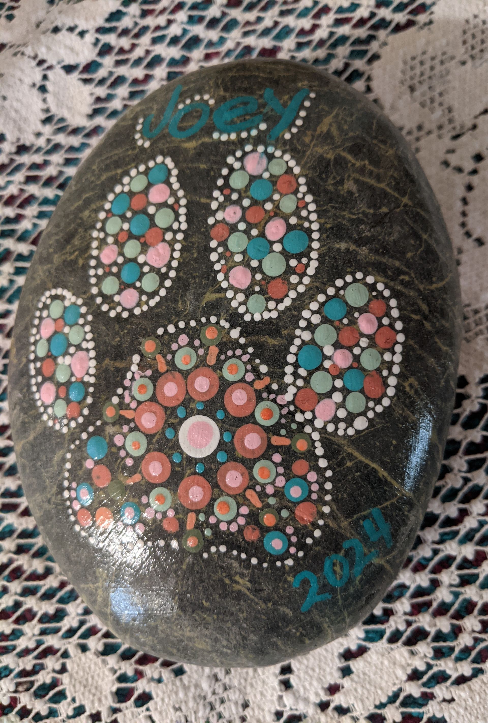 Painted black stone with colorful paw print and “boy 2024” on a lace background