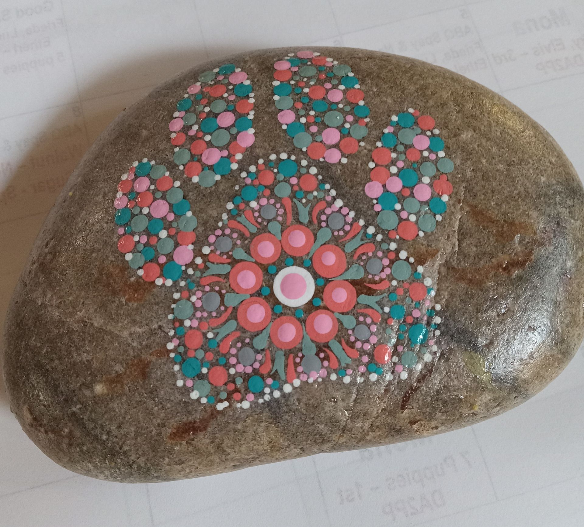 Painted stone with a colorful floral mandala in pink, teal, and white on a brown rock