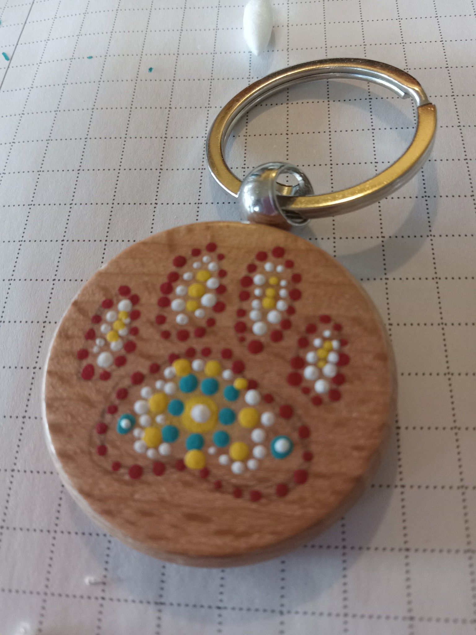Round wooden paw-print keychain with colorful rhinestones on a gridded surface