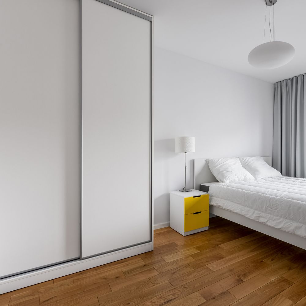 Bedroom With White Closet, Bed, Yellow Nightstand, Wood Floor, and Gray Curtains — Sams Glass Solutions in Airlie Beach, QLD