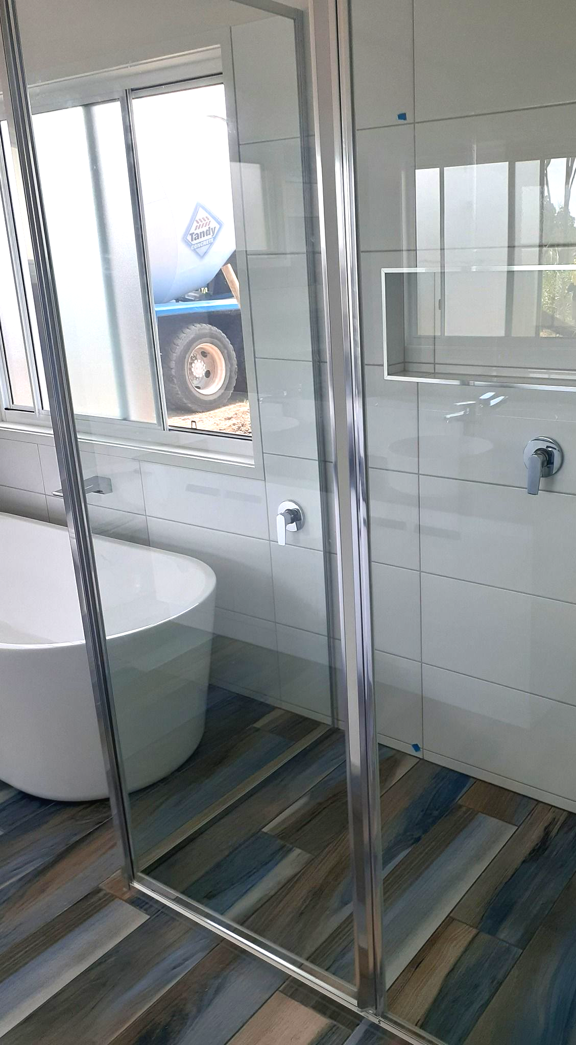 A Modern Bathroom With Light Grey Marble Tiles, a Freestanding White Bathtub — Sams Glass Solutions in Proserpine, QLD