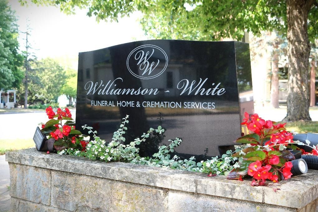 A black stone monument for Williamson-White Funeral Home & Cremation Services, surrounded by red flowers and greenery.