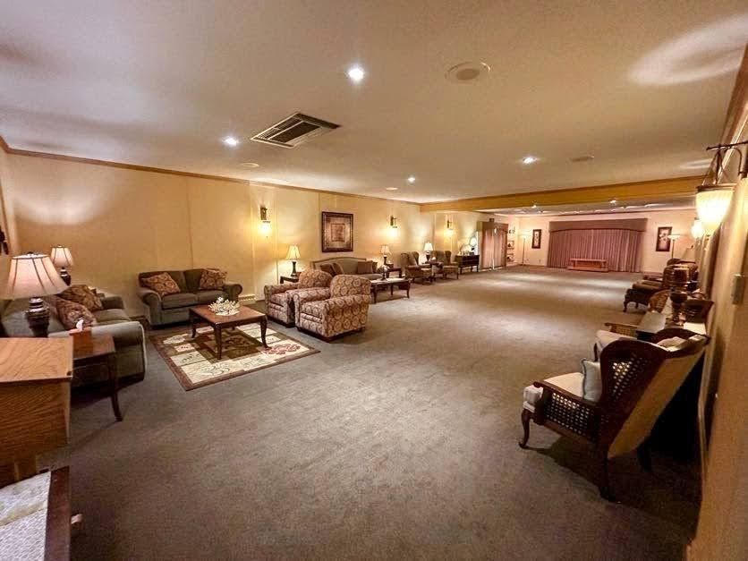 A spacious, dimly lit room with carpeted floors, arranged with sofas and armchairs for seating, leading to a stage area.