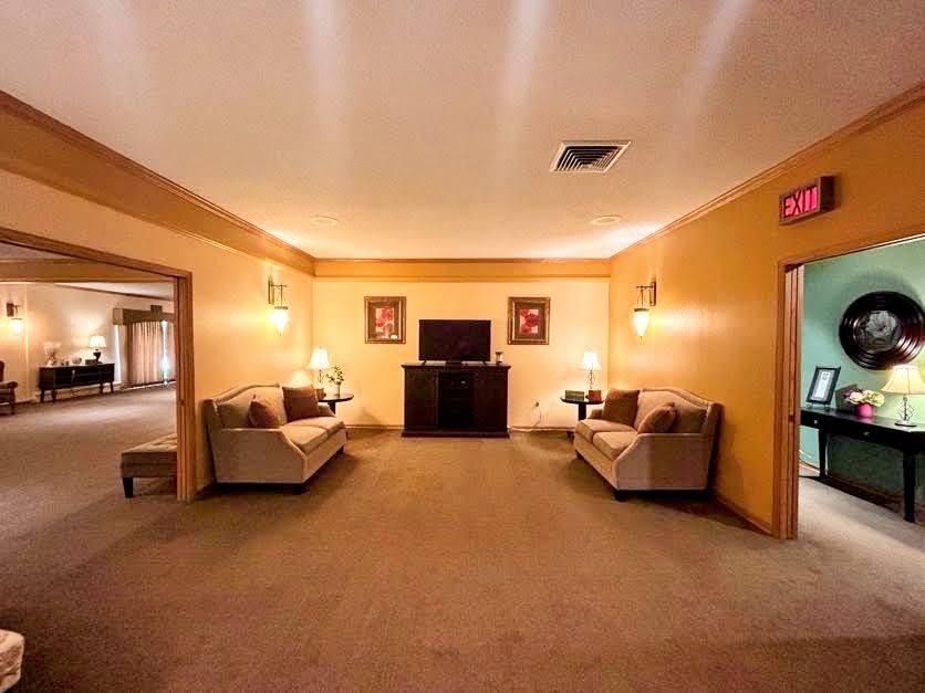 A symmetrical lounge with beige couches facing a central television, flanked by doorways leading to other rooms.