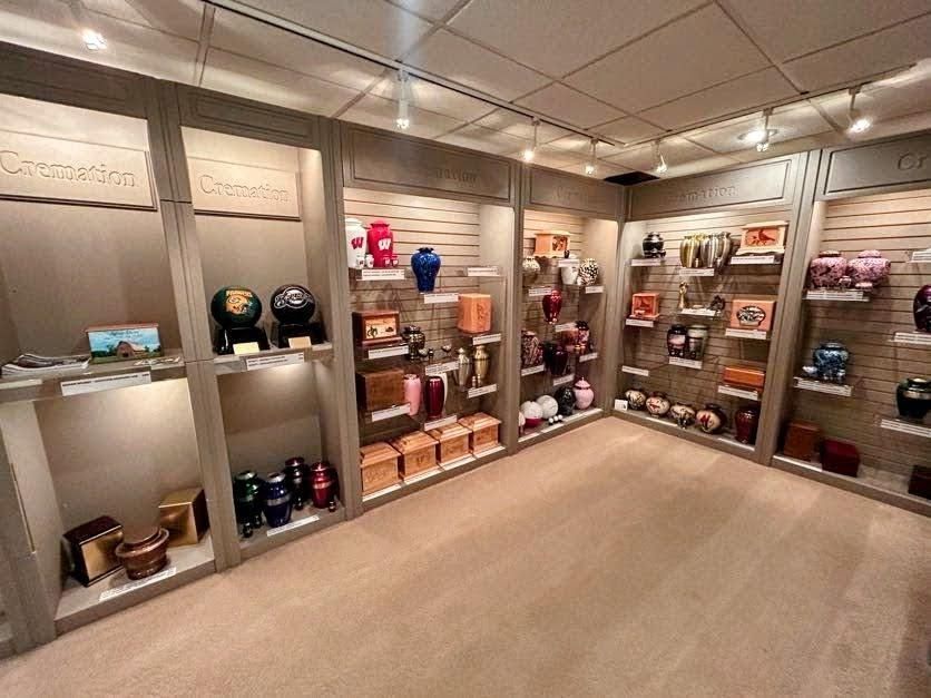 A showroom display of various urns and funeral memorial products arranged on shelves in a brightly lit, neutral room.