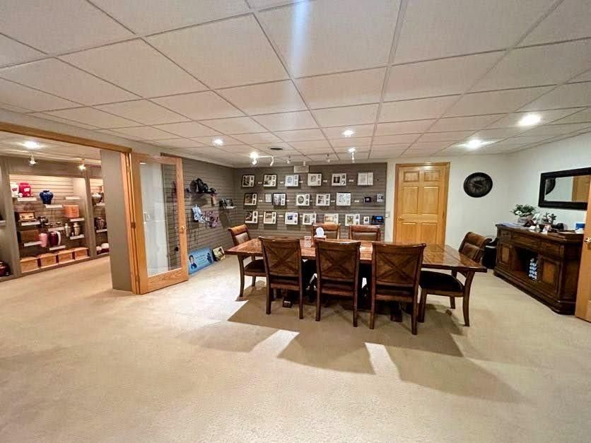 A wood-toned dining table and chairs sit in a finished basement with a display wall, recessed lighting, and a side buffet.