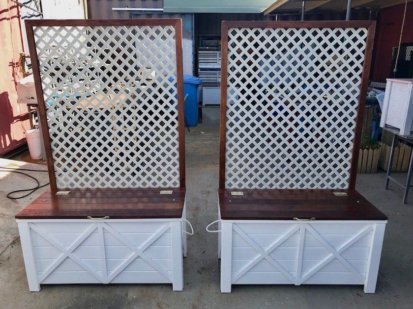Two white lattice garden panels mounted on brown and white planter boxes outdoors.