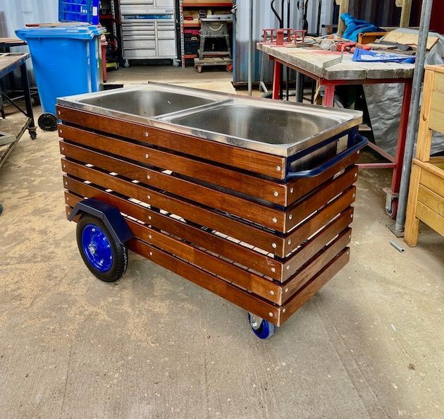 Wooden utility cart with double stainless-steel sink and blue wheels in a workshop