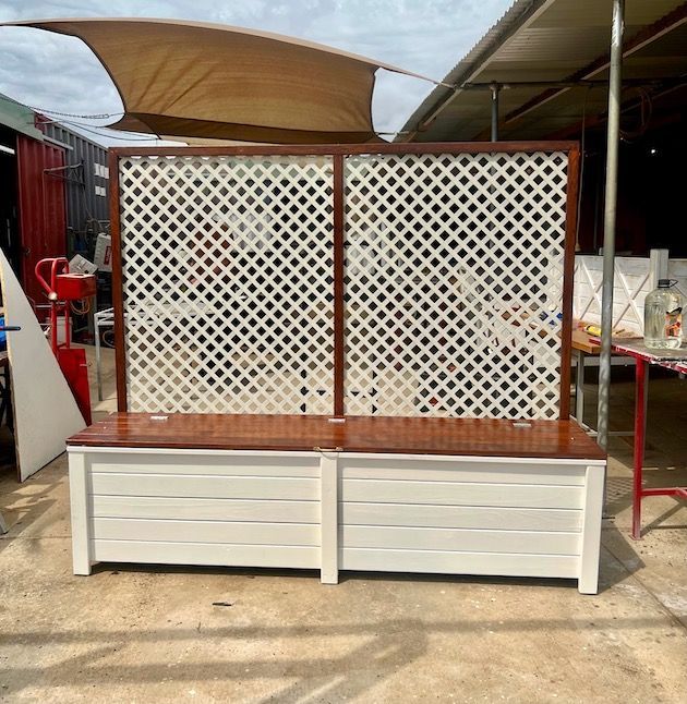 White lattice bench with wooden top in an outdoor market area under awnings