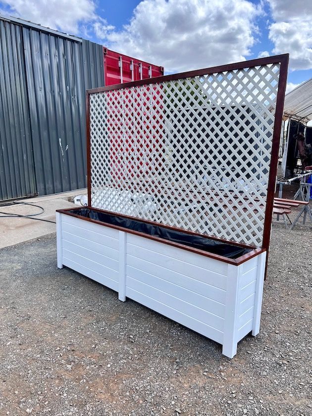 White planter box with brown lattice trellis outdoors beside shipping containers.