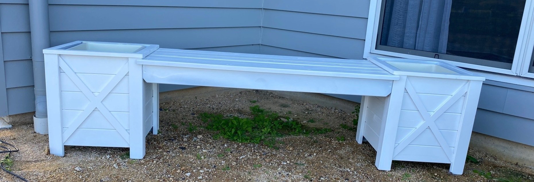 White wooden bench between two white storage boxes against a gray house wall