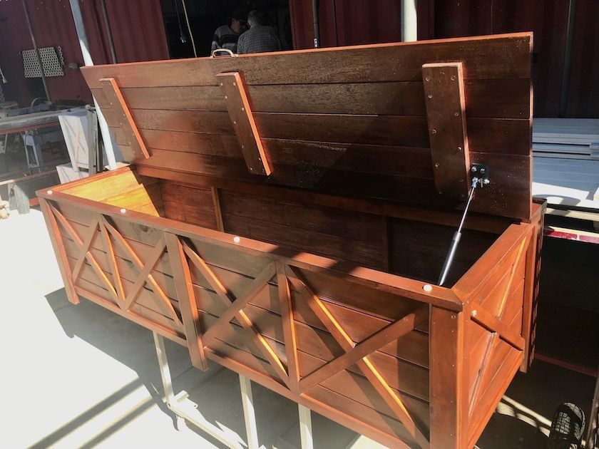 Wooden storage chest with open lid, rustic brown finish, and crisscross front panels in bright sunlight