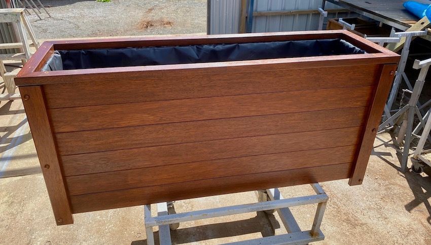 Wooden planter box with dark interior, sitting on a stand outdoors.