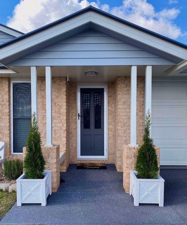 Front porch with blue front door, white columns, brick walls, and potted shrubs by the entrance