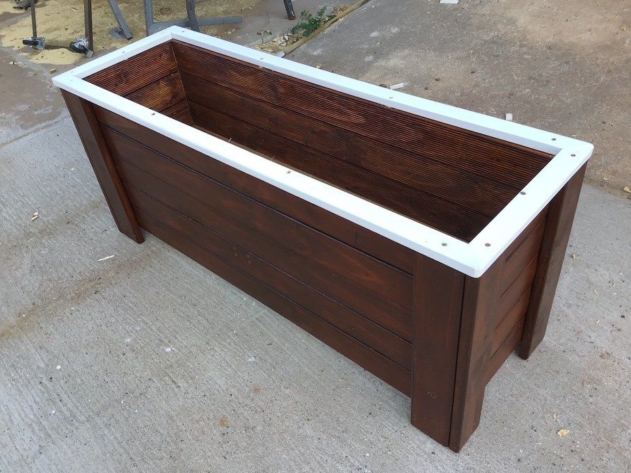 Wooden planter box with white top trim, sitting on a concrete surface outdoors