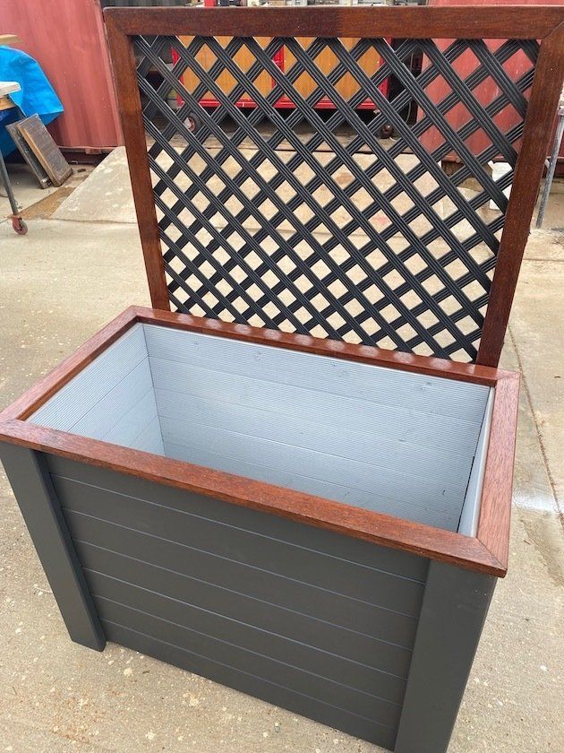 Open wooden storage bench with black sides and lattice backrest in a workshop setting