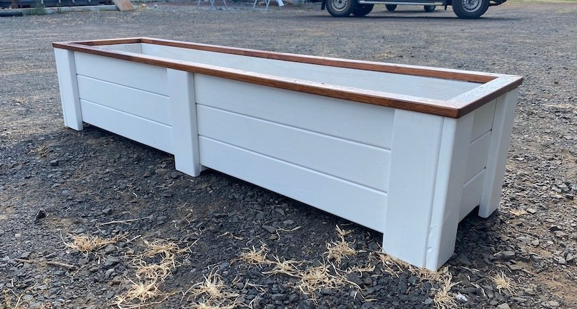 White wooden outdoor bench with a brown top, shown on gravel.