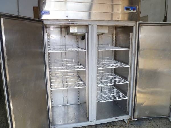 Frigorifero commerciale in acciaio inox con porte aperte e ripiani interni.