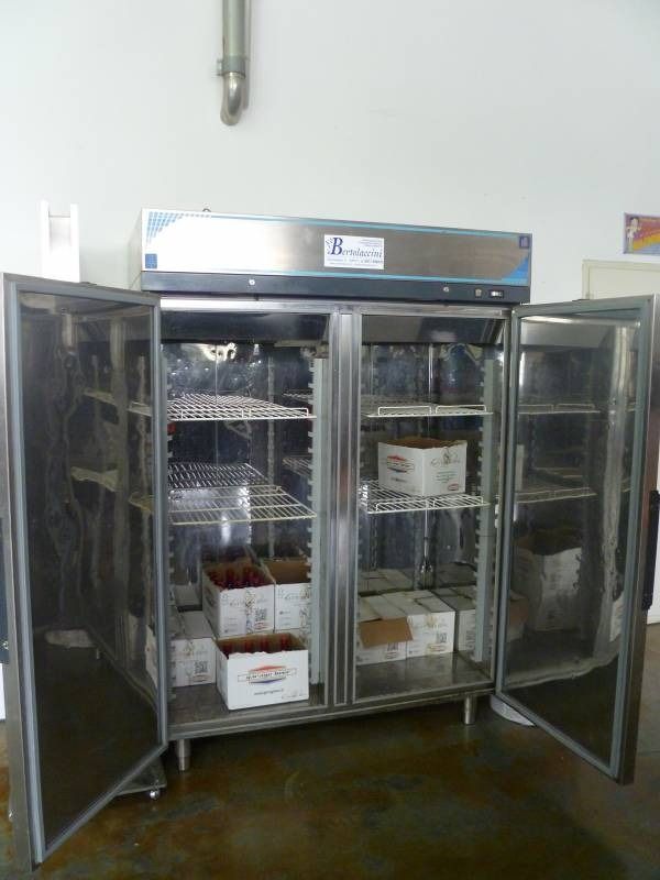 Un frigorifero commerciale in acciaio inossidabile con due porte aperte, pieno di scatole e ripiani.
