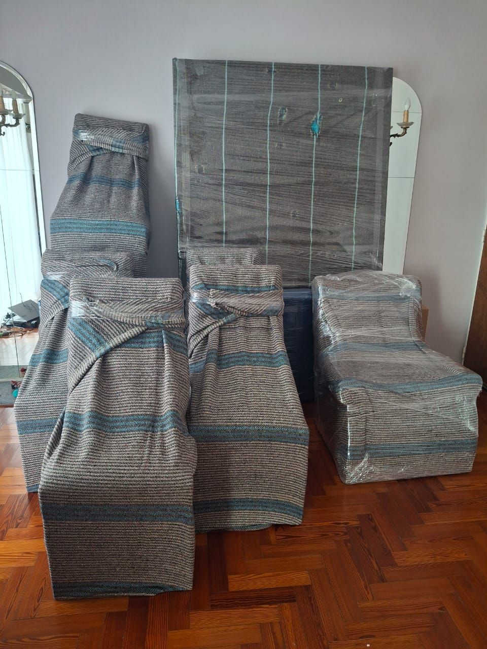 Muebles apilados, envueltos en plástico y mantas, en una habitación con suelo de madera.