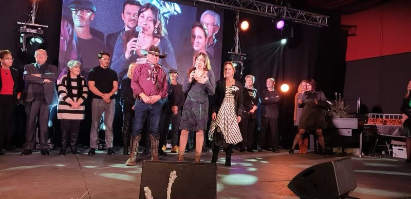 Des personnes sur scène avec des microphones, un grand écran en arrière-plan, un projecteur et une scène.