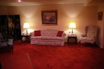 A living room with a patterned sofa, two lamps on side tables, and a floral armchair on bright red carpet.