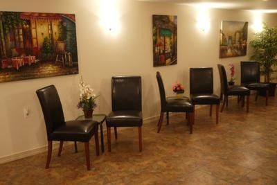 A waiting area with five dark chairs, wall art, small side tables with flowers, and tiled floors.