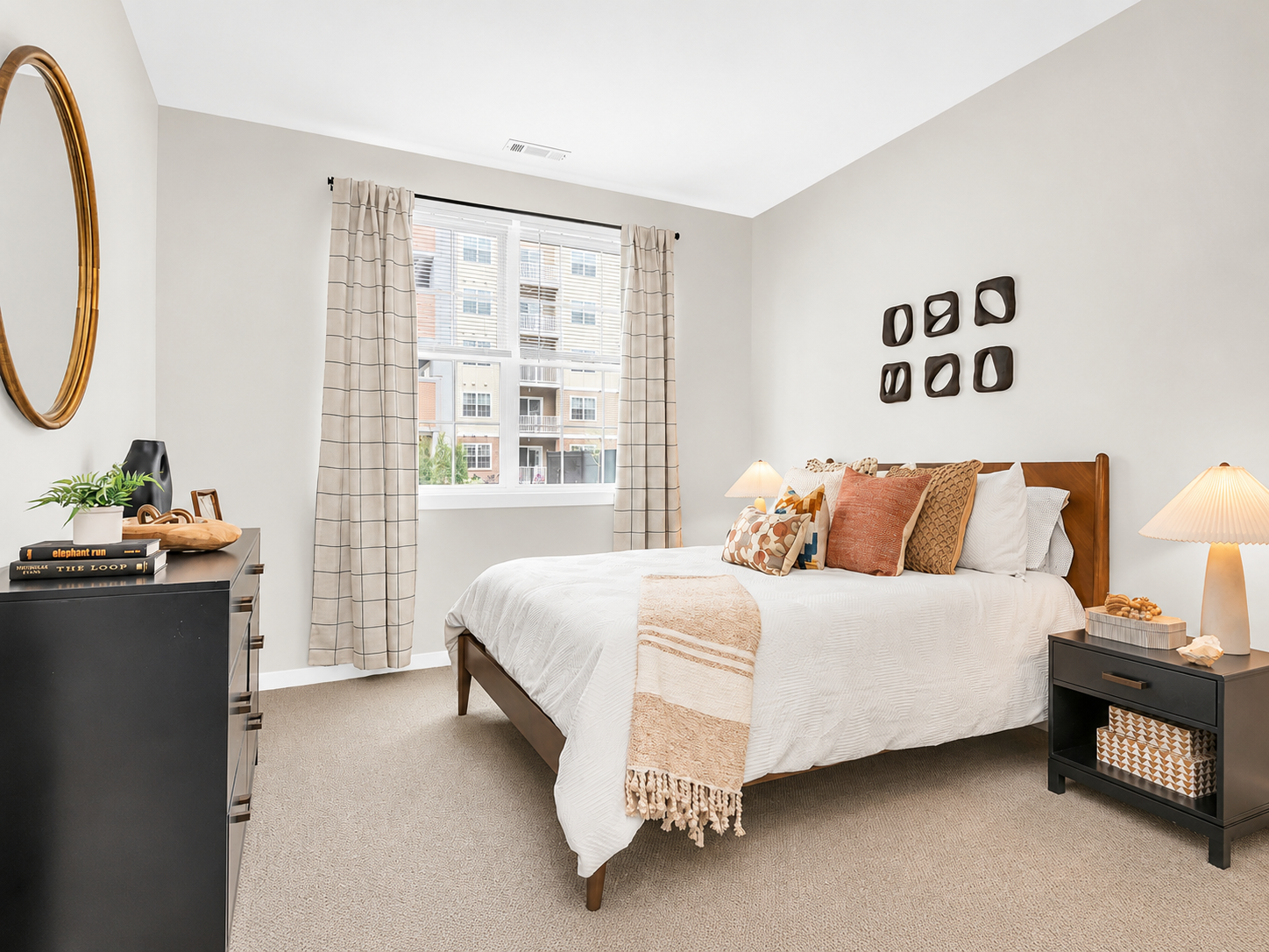 Bedroom with beige upholstered bed, nightstand, lamp, and window blinds.