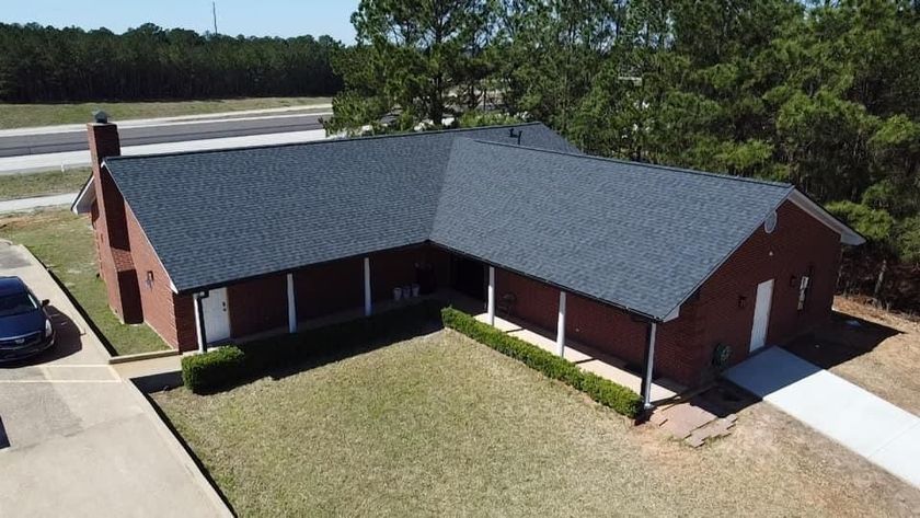 Brick house with dark roof and white trim, front porch, and driveway on a grassy lawn.