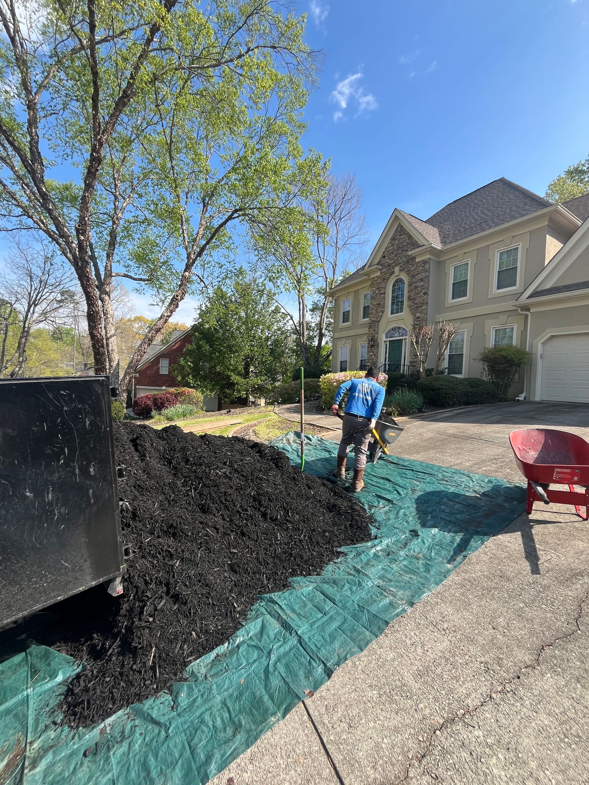 A man is standing next to a large pile of mulch in front of a house.