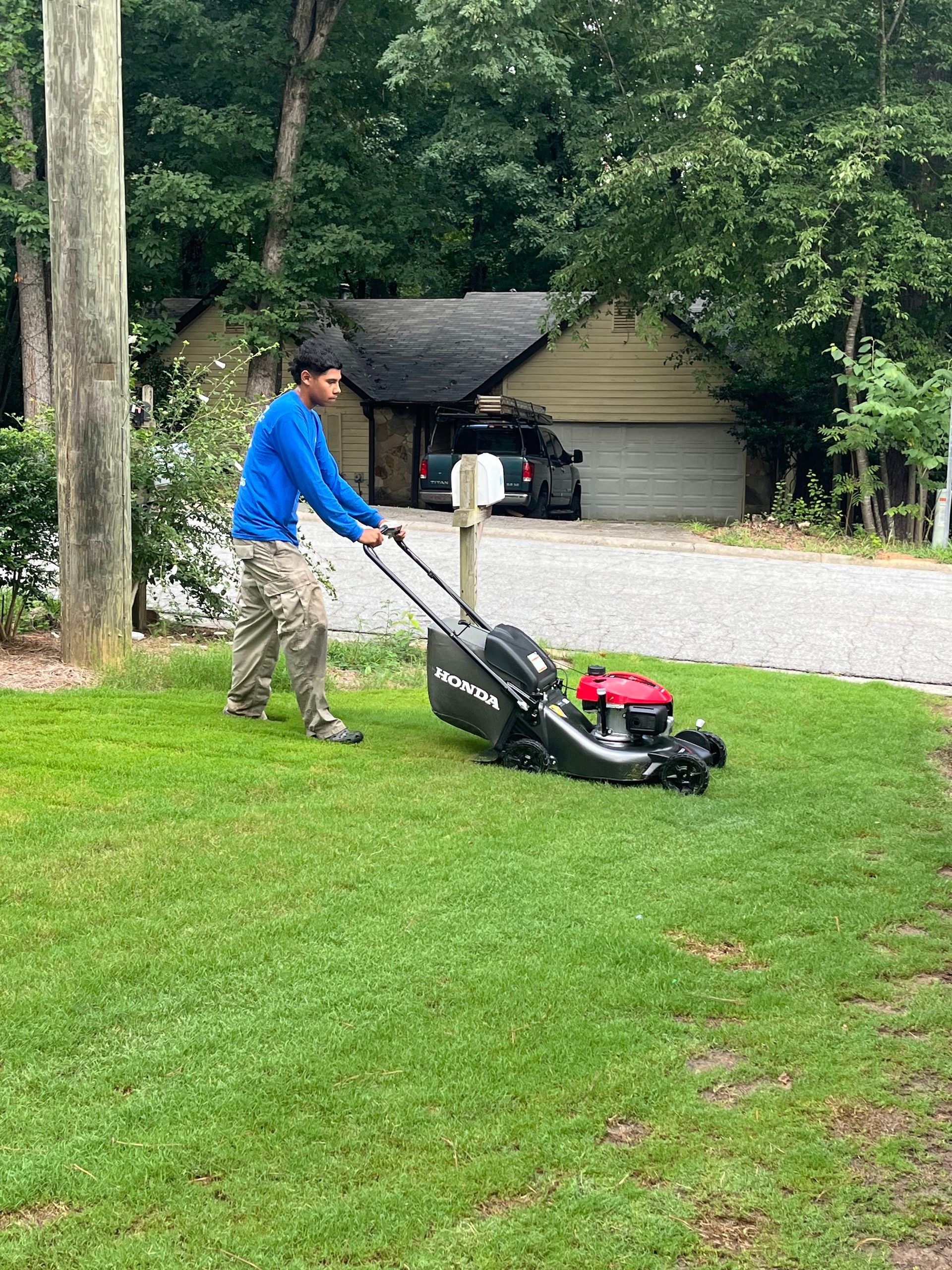 A man is using a lawn mower to cut the grass in front of a house.