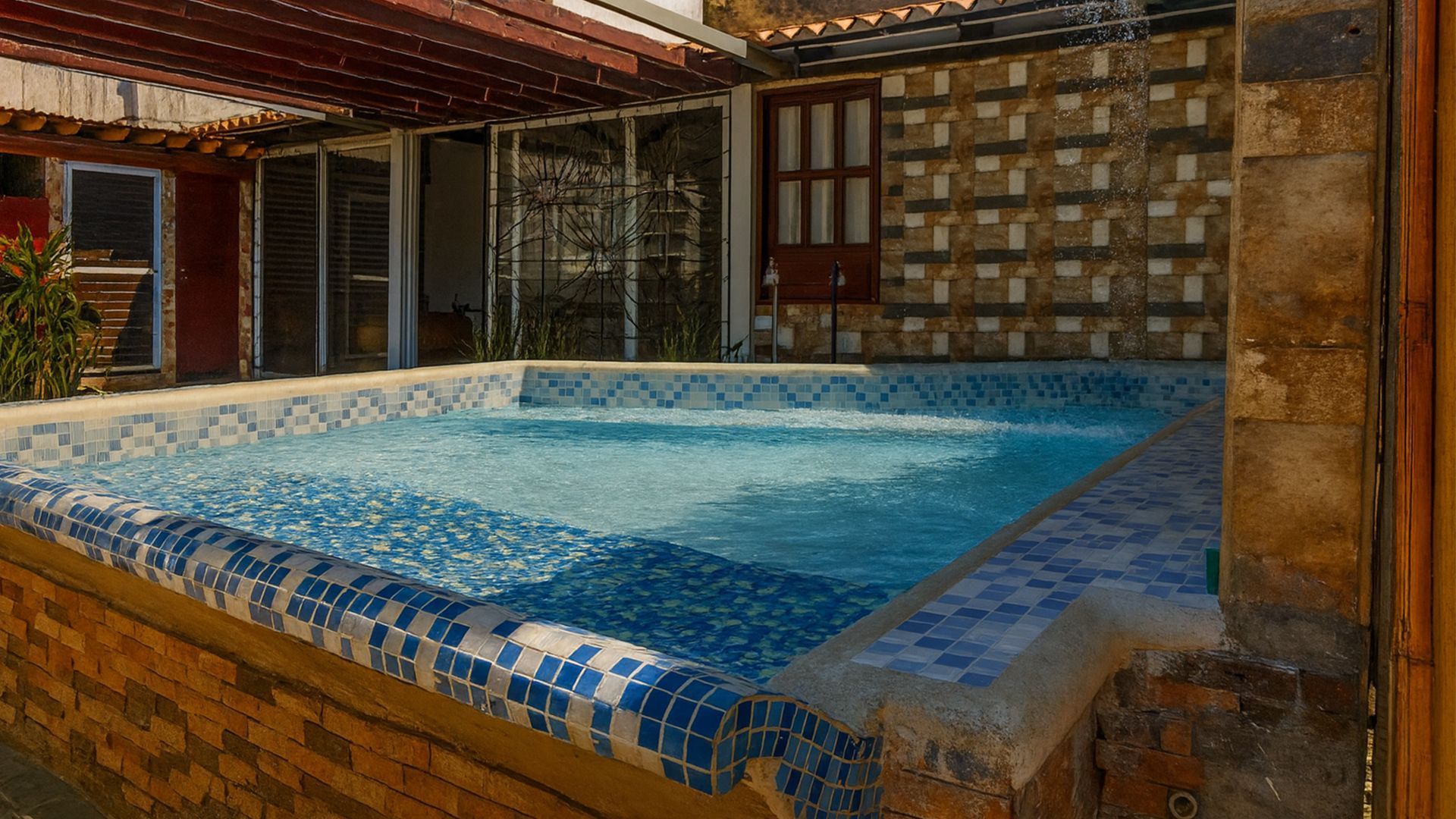 Pequeña piscina cubierta con azulejos y agua azul en un entorno de patio rústico.