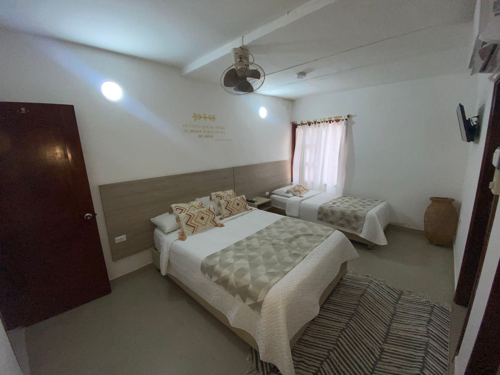 Habitación pequeña con dos camas, paredes blancas y una ventana con cortinas rosas.