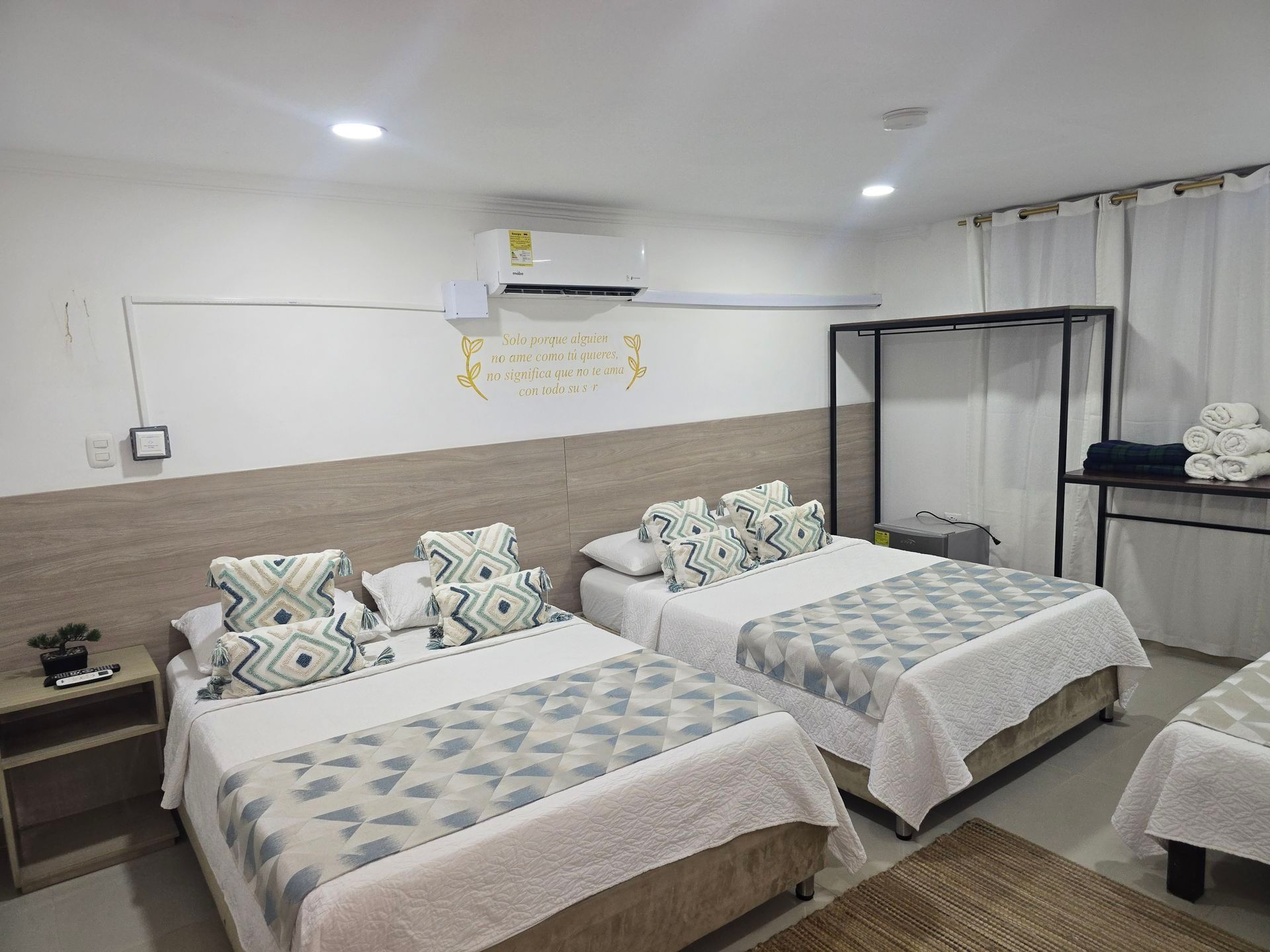 Habitación luminosa con dos camas individuales, detalles en madera y un perchero negro sobre paredes blancas.
