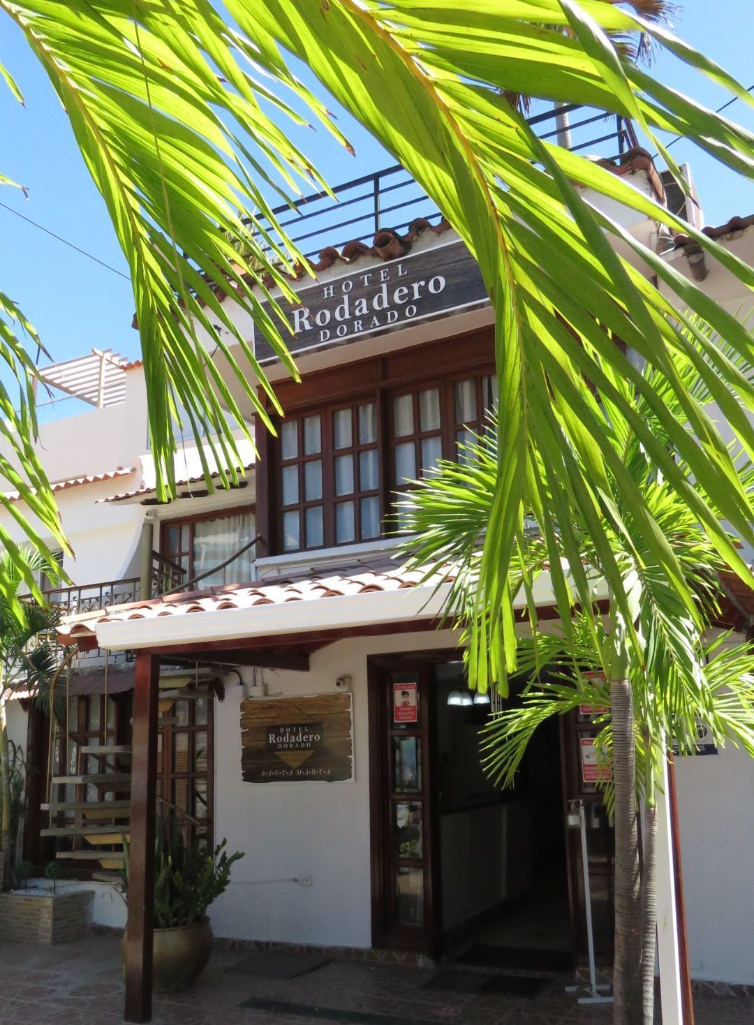 Pequeña fachada blanca de restaurante con ventanas de madera y hojas de palma al frente, letrero que dice “Reddadero”.