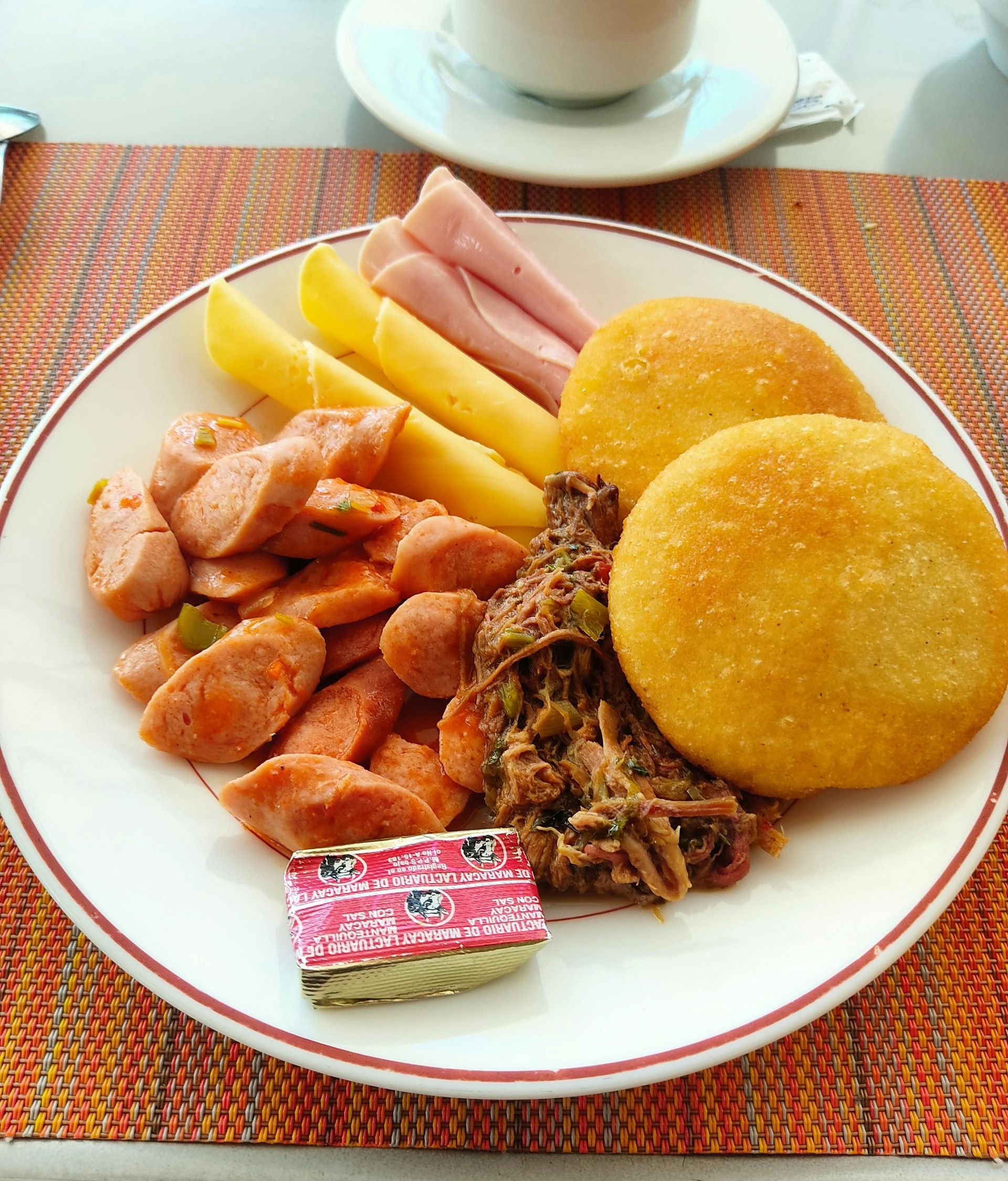 Plato de desayuno variado con alimentos fritos, fruta y tortas de maíz sobre un mantel individual tejido.