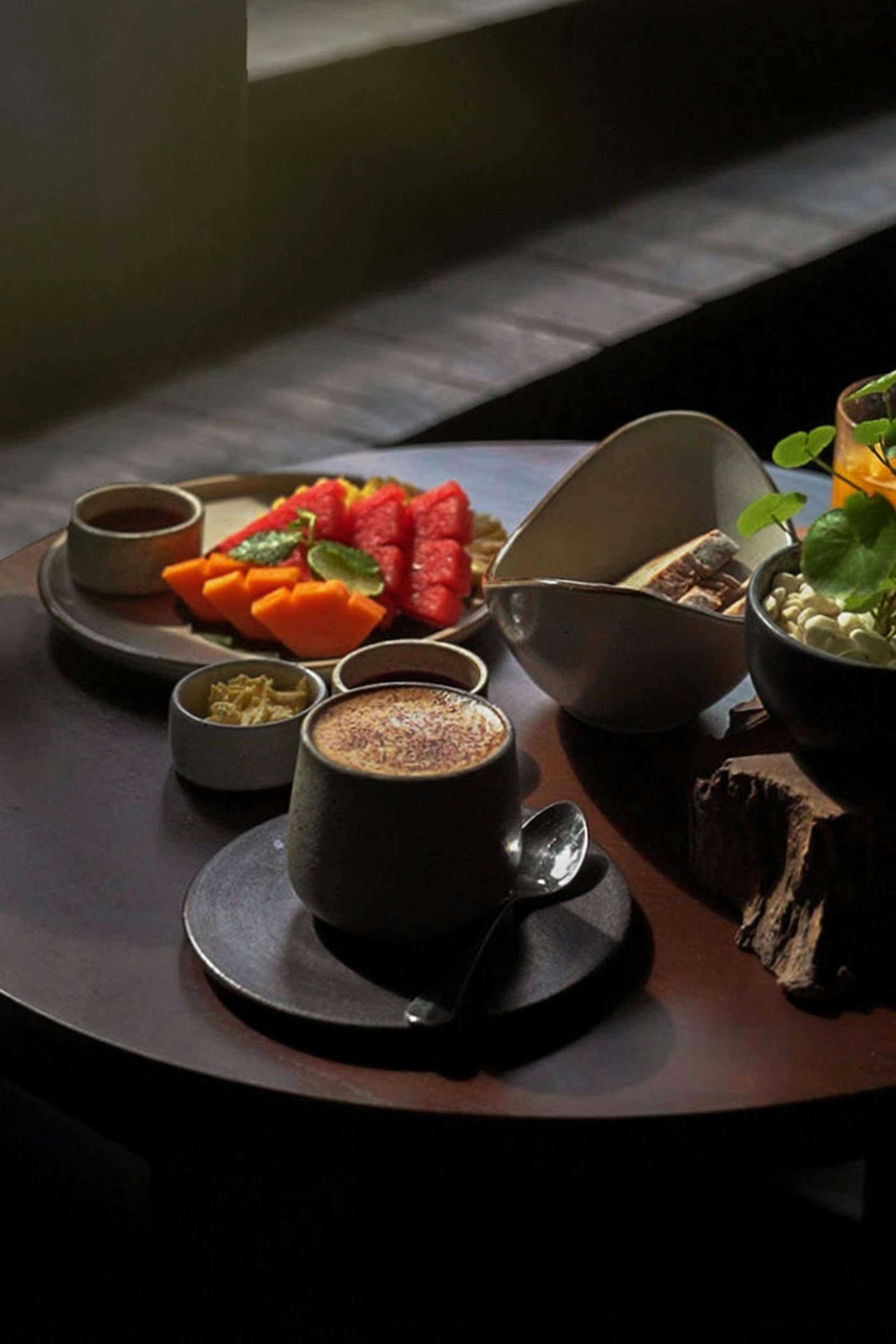 Bandeja de desayuno con café, zumo de naranja, fruta, ensalada y pan bajo una suave luz solar.