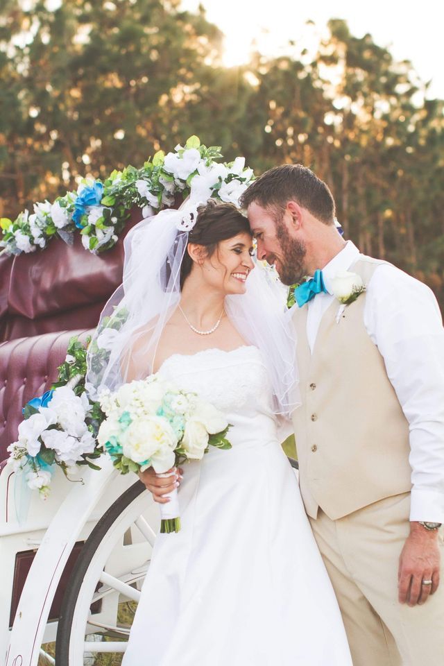 A bride and groom are posing for a picture in front of a horse drawn carriage.