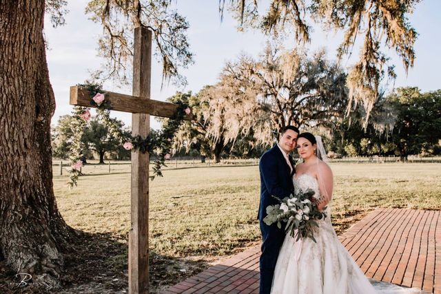A bride and groom are posing for a picture in front of a wooden cross.