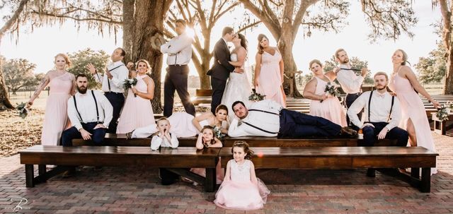 A wedding party is posing for a picture on a wooden bench.