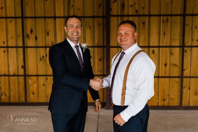 Two men are shaking hands in front of a wooden wall.