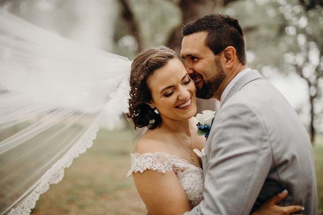 A bride and groom are posing for a picture with their veil blowing in the wind.